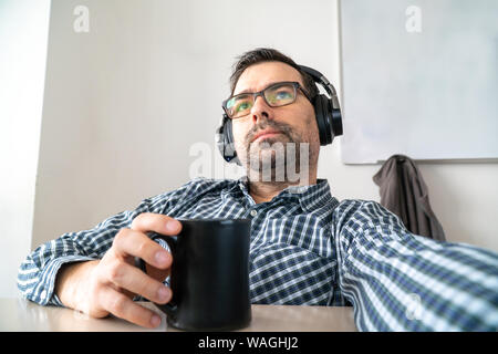 Homme d'âge moyen concentré à la recherche sur l'écran d'un ordinateur tout en travaillant et tenant une tasse de café dans sa main Banque D'Images