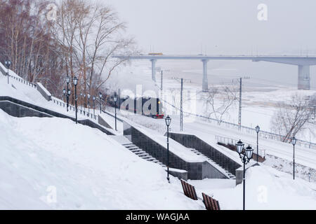 Paysage de neige d'hiver avec locomotive à vapeur se déplaçant le long de la rivière avec le pont automobile dans l'arrière-plan Banque D'Images