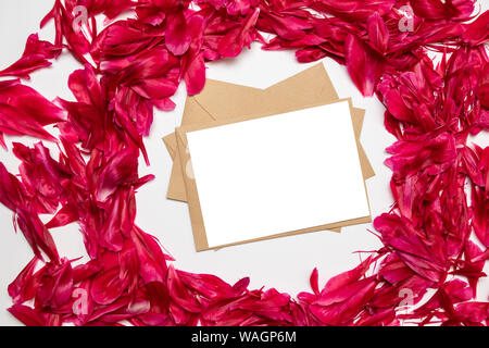 Le papier blanc et de l'enveloppe rouge avec pétales de pivoines sur fond gris. Concept créatif, modèle de carte de vœux. L'horizontale Banque D'Images