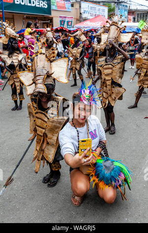 Une jeune femme portant un chapeau de fête traditionnelle prend une des Selfies elle-même et un enfant dans la Procession, Ati-Atihan Festival, Kalibo, Philippines. Banque D'Images