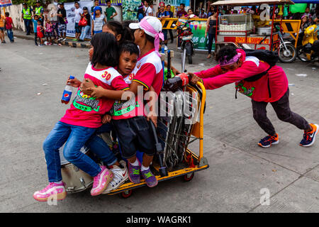 Un jeune homme pousse un groupe d'enfants autour de sur un chariot, l'Ati-Atihan Festival, Pamukkale, l'Île Panay, Province d'Aklan, Philippines. Banque D'Images