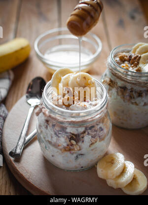 Close-up de l'avoine à la banane fait maison dans un bocal en verre avec du miel des gouttes, sur fond de bois Banque D'Images