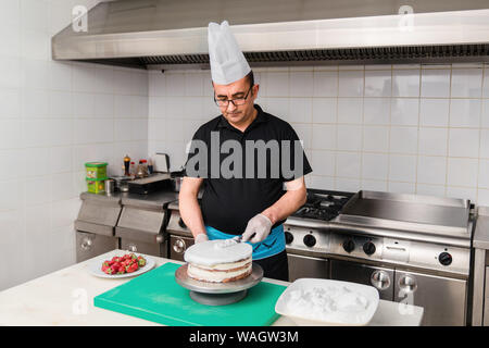 Male chef pâtissier faire un gâteau avec une cerise. concept processus de production chez les clients pour commander des gâteaux maison. Banque D'Images