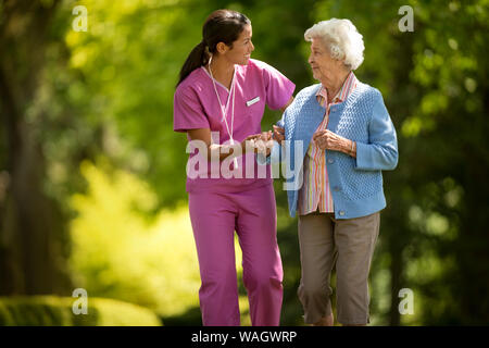 Heureux jeune infirmière utilement aider un patient âgé à marcher à l'extérieur. Banque D'Images