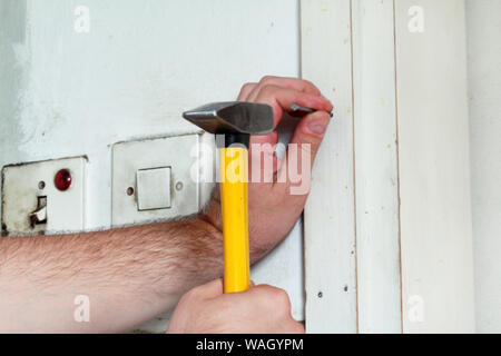 Travailleur de la construction et l'homme à travailler sur des travaux de rénovation. Builder avec marteau frappe jaune et des ongles un clou dans le mur en bois de porte de la cuisine. Banque D'Images