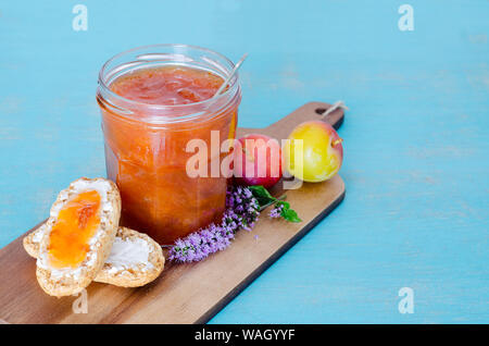 Confiture de prunes maison dans un bocal en verre avec des toasts et des prunes sur table en bois et fond bleu. Banque D'Images