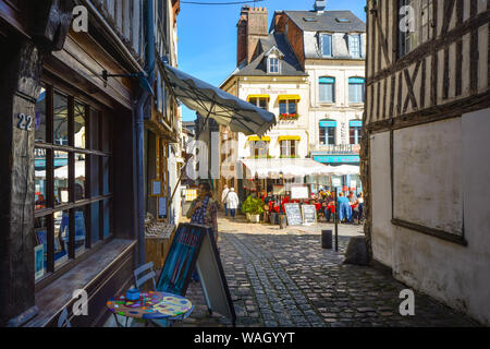 Une femme boutiques fenêtre sur une journée ensoleillée dans la ville de Honfleur Normandie France avec une piscine sidewalk cafe derrière elle Banque D'Images