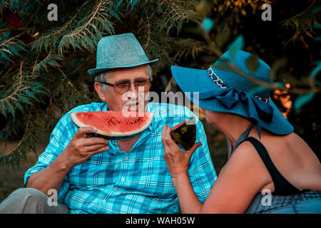 Happy senior couple aimant eating watermelon et avoir un grand temps ensemble sur un pique-nique dans le parc. Banque D'Images