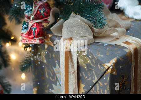 Close up of a joliment emballé et attaché avec un ruban de dentelle d'or don dans l'arbre de Noël, selective focus Banque D'Images