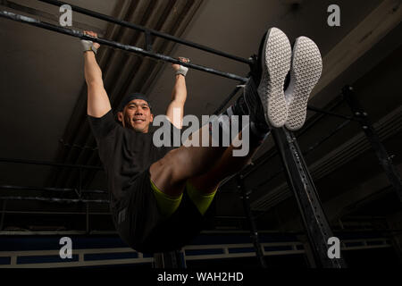 Un beau jeune homme avec les muscles est souriant et faisant l'exercice l'asseoir sur la barre horizontale. Fitness fonctionnel d'entraînement dans une salle de sport. Banque D'Images