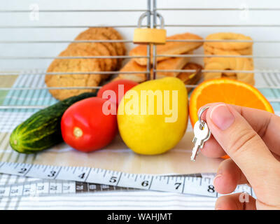La femme détient la clé de la cellule avec les cookies. Les témoins sont dans la cage avec un cadenas verrouillé. La saine alimentation et de l'interdiction de junk food concept. Banque D'Images