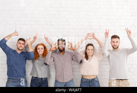 Happy friends gesturing with hands over white brick wall Banque D'Images