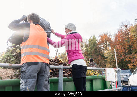 La femme et l'homme dans le récipient vert déchets donnant sur le centre de recyclage Banque D'Images