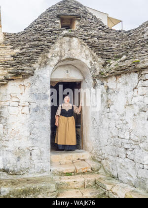 L'Italie, l'Alberobello. Femme en vêtements traditionnels en porte. Banque D'Images