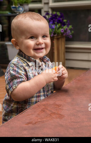 Issaquah, Washington State, USA. Quatorze mois heureux Bébé Garçon jouant avec une carotte en plastique à l'extérieur, à l'aide d'une couverture du spa pour une table. (Monsieur,PR) Banque D'Images