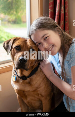 Issaquah, Washington State, USA. 12 ans, fille, et l'étreindre Fox Red Labrador à côté d'une fenêtre. (MR, communication) Banque D'Images