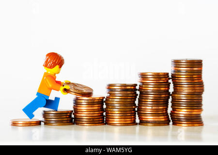 Concept d'économie d'argent - une figurine jouet transportant des pièces de monnaie dans une pile de pièces. Banque D'Images