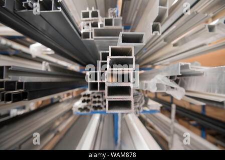 Longueurs fraisées de profilés extrudés en alliage d'aluminium (aluminium) assis sur des rayonnages dans un entrepôt et éclairés par la lumière naturelle Banque D'Images