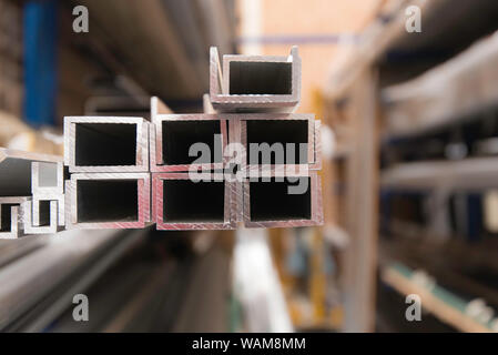 Longueurs fraisées de profilés extrudés en alliage d'aluminium (aluminium) assis sur des rayonnages dans un entrepôt et éclairés par la lumière naturelle Banque D'Images