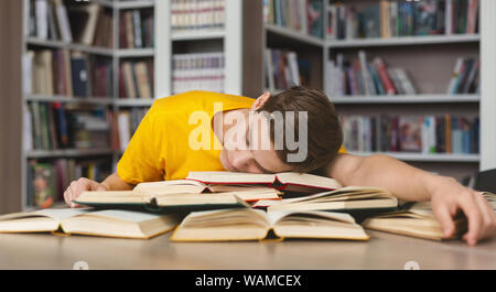 Fatigué guy sieste sur books in library Banque D'Images