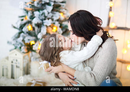 Belle mère heureuse avec petits lher fille en pull tricoté assis sur l'arrière-plan d'intérieur de Noël ensemble et étreindre smiling Banque D'Images