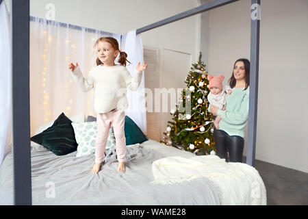 Belle mère heureuse avec petits lher fille en pull tricoté assis sur l'arrière-plan d'intérieur de Noël ensemble et étreindre smiling Banque D'Images