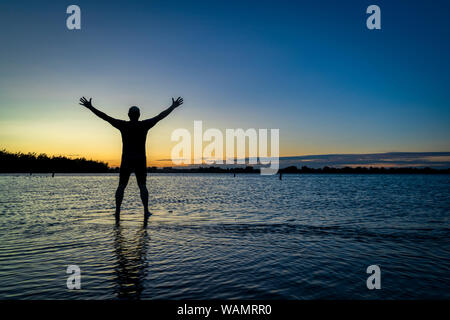 Lever du soleil silhouette d'un homme debout dans l'eau peu profonde et l'étirement ou la pratique de mouvements chigong, Boyd Lake State Park dans le nord du Colorado Banque D'Images