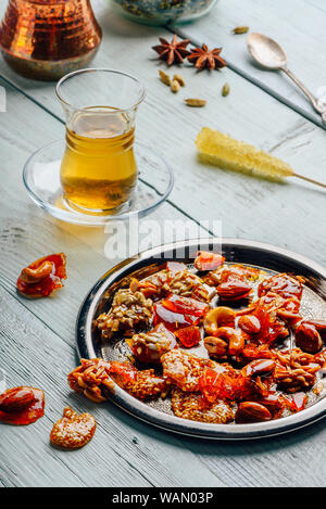 Oriemtal avec différents délices noix et graines sur plaque de métal avec du thé vert en verre armudu sur surface en bois clair Banque D'Images