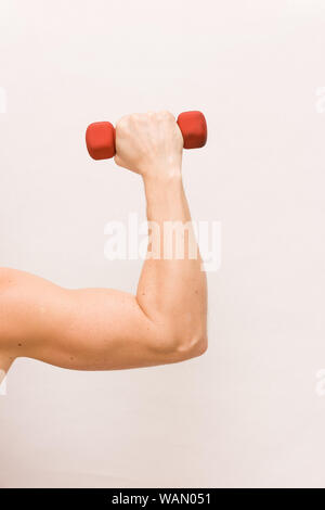 Close-up of strong man's arm holding petit haltère rouge sur fond blanc. Concept de remise en forme et de santé. Main pliée à l'équerre, tenant un haltère. M Banque D'Images