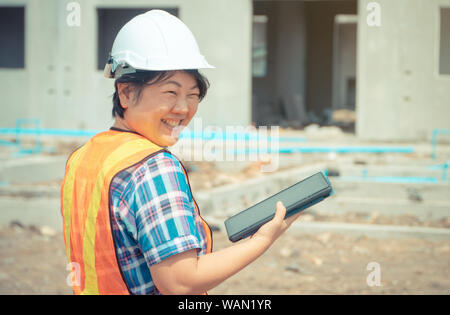 Les femmes asiatiques engineering est titulaire d'une tablette pour une utilisation dans l'inspection des chantiers de construction pour plus de précision et en conformité avec le plan. Concept de l'égalité de Banque D'Images