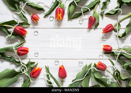 Frontière avec printemps tulipes rouges, perle blanche et la chaîne de pierres en verre disposées en cercle sur fond de bois blanc Banque D'Images