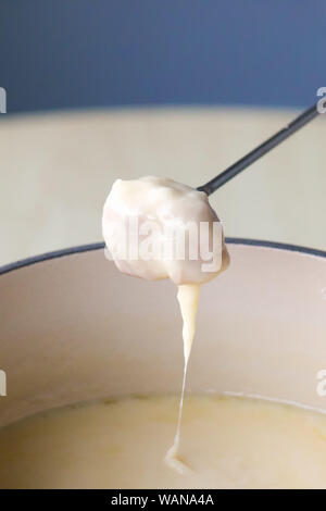Plat traditionnel suisse - fondue au fromage. La baguette sur une fourchette à fondue est trempé dans du fromage fondu. Servi dans un pot commun chauffé avec une bougie ou une lampe à alcool. Close up photo. Photo verticale. Banque D'Images