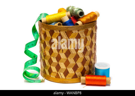 Boîte de forme cylindrique en écorce manuellement tressée avec des bobines de fils colorés de couturière et ruban à mesurer, isolé sur fond blanc Banque D'Images