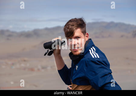 La Mongolie Ulgii 2019-05-04 European Jeune homme regardant à travers des jumelles. Voyageur solitaire Concept, backpacker en montagne, randonnées, escalade, randonnée pédestre Banque D'Images