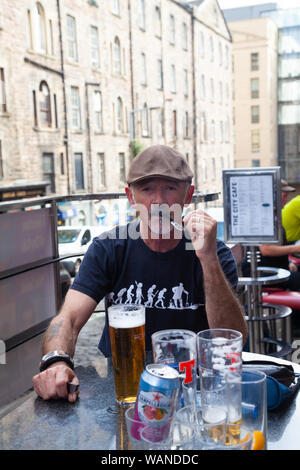 Un homme d'âge moyen fumant une pipe à l'extérieur avec une pinte de bière blonde en face de lui. Banque D'Images