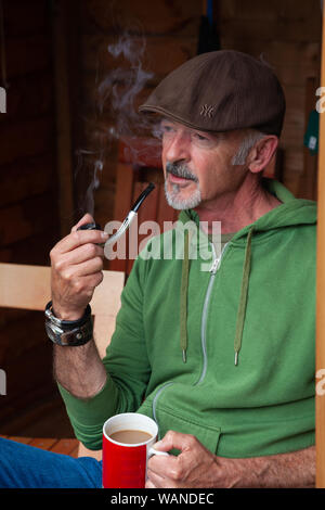 Un homme d'âge moyen assis dans un hangar et fumer une pipe. Banque D'Images