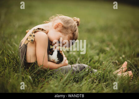 Petite fille se blottissant son animal de cobaye dans l'herbe Banque D'Images