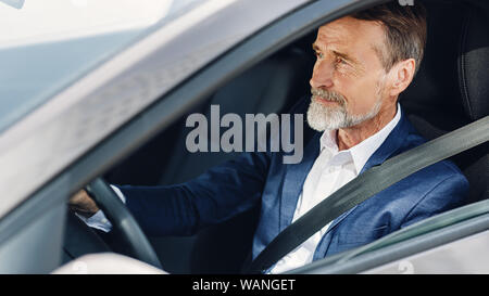Vue latérale d'un homme d'âge mûr. Le plus âgé se concentrant sur la route tout en conduisant une voiture. Banque D'Images