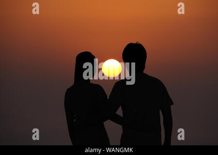 Vue arrière d'un couple embrassant regardant le coucher du soleil Banque D'Images