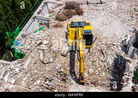 Les machines de la pelleteuse travaillant sur le site de la démolition d'un vieux building workers pulvériser de l'eau pour se débarrasser de la poussière. Banque D'Images