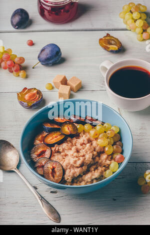 Petit-déjeuner sain concept. Porridge avec prunes fraîches, raisins verts et tasse de café. Sur fond de bois des ingrédients. Banque D'Images