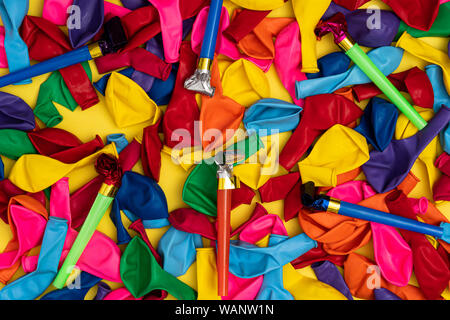 Partie des sifflets et des ballons dégonflés, mise à plat. Partie de couleur des sifflets et colorés ballons dégonflés sur fond jaune, vue du dessus. Stock photo pour Banque D'Images