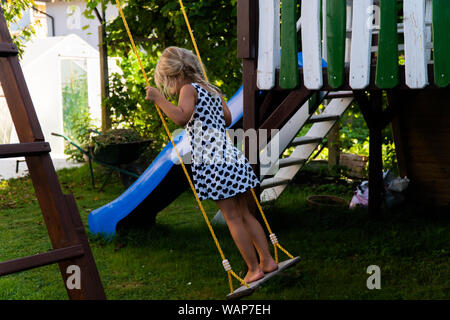 3-5 ans fille blonde s'amusant sur une balançoire à l'extérieur. Jeux d'été. Fille se balançant de haut. Jeune enfant sur la balançoire dans le jardin Banque D'Images