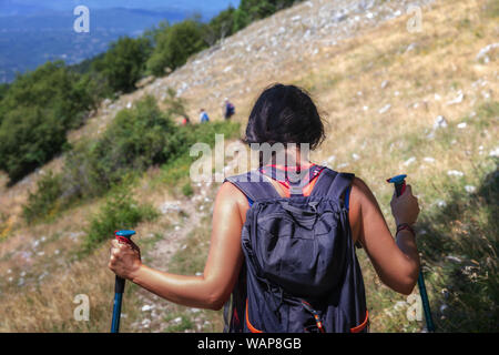 Fille randonneur promenades sur le sentier de montagne, portant son sac à dos sur son épaule. Un jour d'été. De derrière Banque D'Images