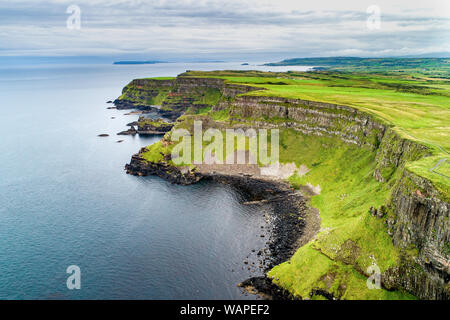 L'Irlande du Nord, Royaume-Uni. Falaises de la côte atlantique dans le comté d'Antrim avec strates géologiques visibles, et formation de basalte volcanique naturel de pol hexagonale Banque D'Images