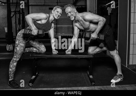 A middle aged couple athlétique et attrayant est en train de faire un entraînement de fitness fonctionnel avec haltères. Homme fort et la femme sont en train de rire dans une salle de sport. Banque D'Images