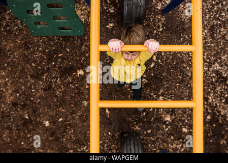 À la recherche sur le jeune garçon traverse monkey bars à jeux pour enfants Banque D'Images