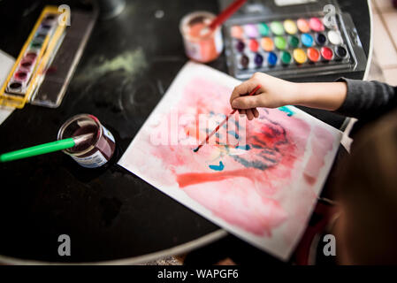 La main du jeune enfant peinture avec un pinceau entouré d'art supplies Banque D'Images