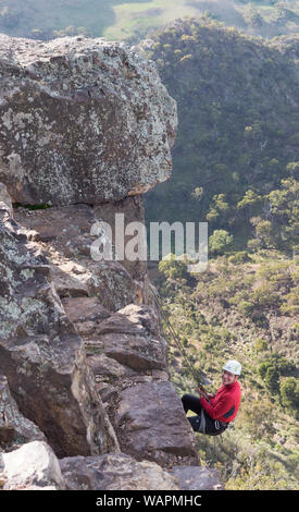 Premier temps technique rock climber hanging off cliff edge alors que la descente en rappel pour la première fois avec rock ledge en premier plan et les montagnes en arrière-plan. Banque D'Images