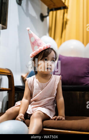 Asian girl fête anniversaire et portant un chapeau rose et tenant un ballon. Banque D'Images